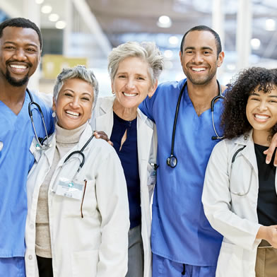 Diverse%20group%20of%20healthcare%20professionals%20smiling%20together,%20wearing%20scrubs%20and%20white%20coats,%20with%20stethoscopes%20around%20their%20necks.