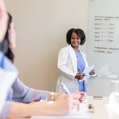 A person in a white coat standing in front of a whiteboard