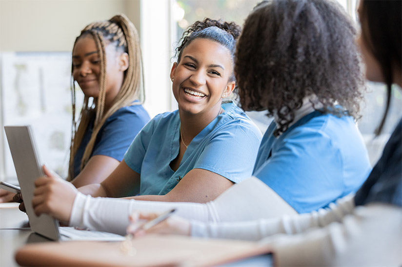 Happy group of multi-cultural nursing staff seated at a conference table, engaged in conversation.