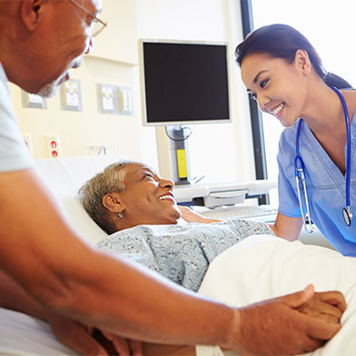 Smiling female medical practitioner attends to smiling patient in hospital bed